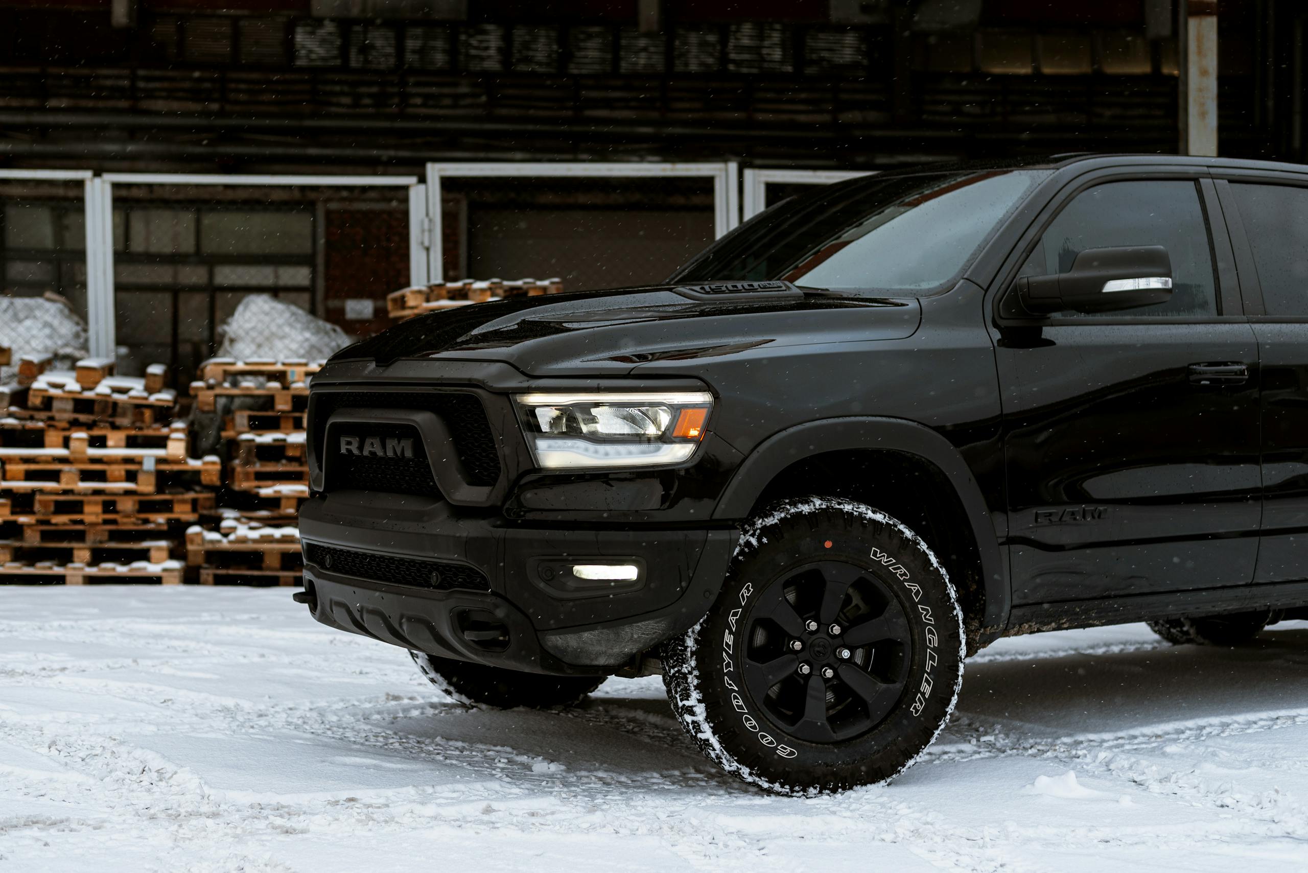 Sleek black pickup truck parked on a snow-covered street, framed by industrial pallets.